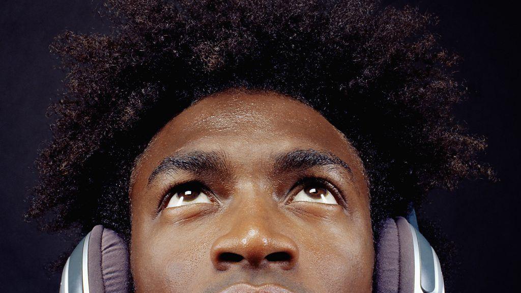 Jovem negro com cabelo afro olha para cima; ele usa fones de ouvido tipo headphones