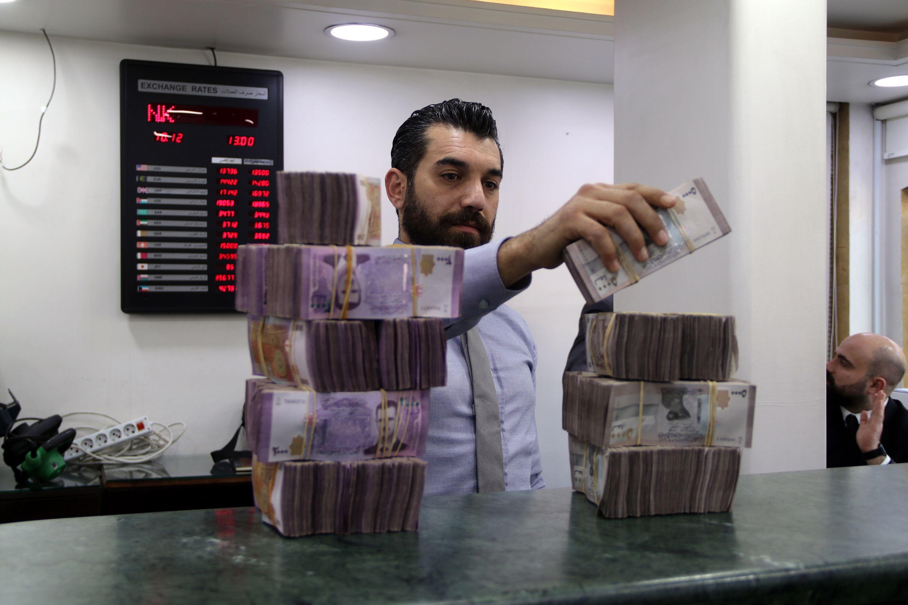 ماذا يعني ارتفاع قيمة اللّيرة السورية؟ 1 موظف يعد الأموال في بنك محلي في دمشق، سوريا، 10 ديسمبر 2024.