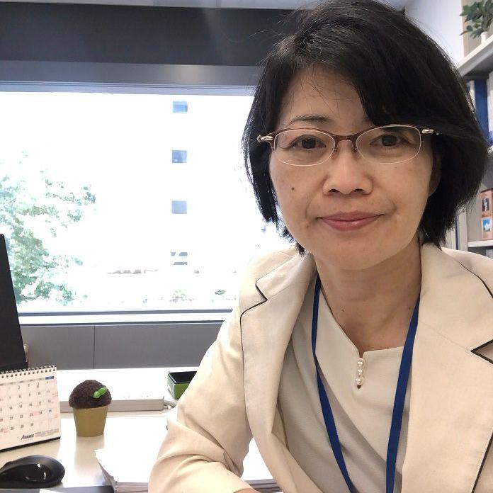 Kazue Matsushita sorrindo em sua mesa de escritório