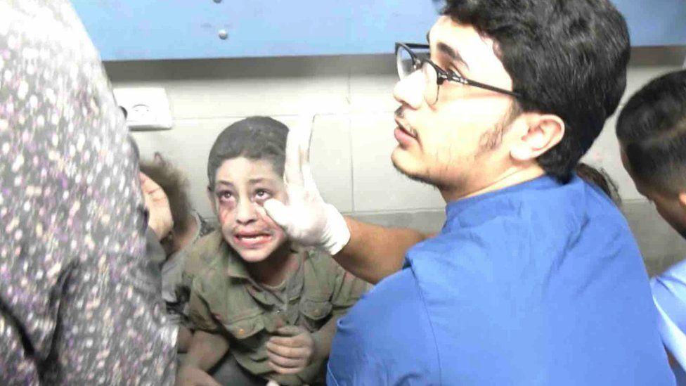 An upset child stares at a woman while a medic tends to him