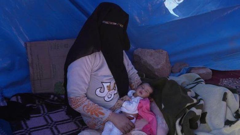 Khadija sostiene en los brazos a su bebé debajo de una lona azul.