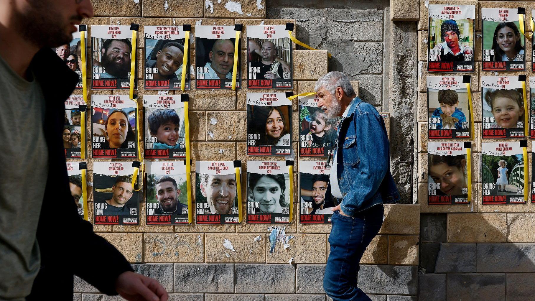 إسرائيليون يسيرون أمام لافتات تحمل صور الرهائن الذين تم اختطافهم في هجوم حماس