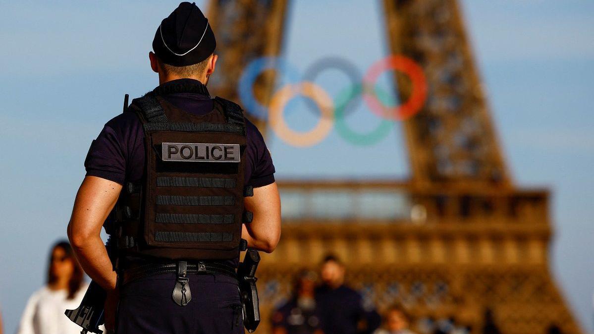 Policial em frente a Torre Eiffel, que está decorada com os arcos olímpicos