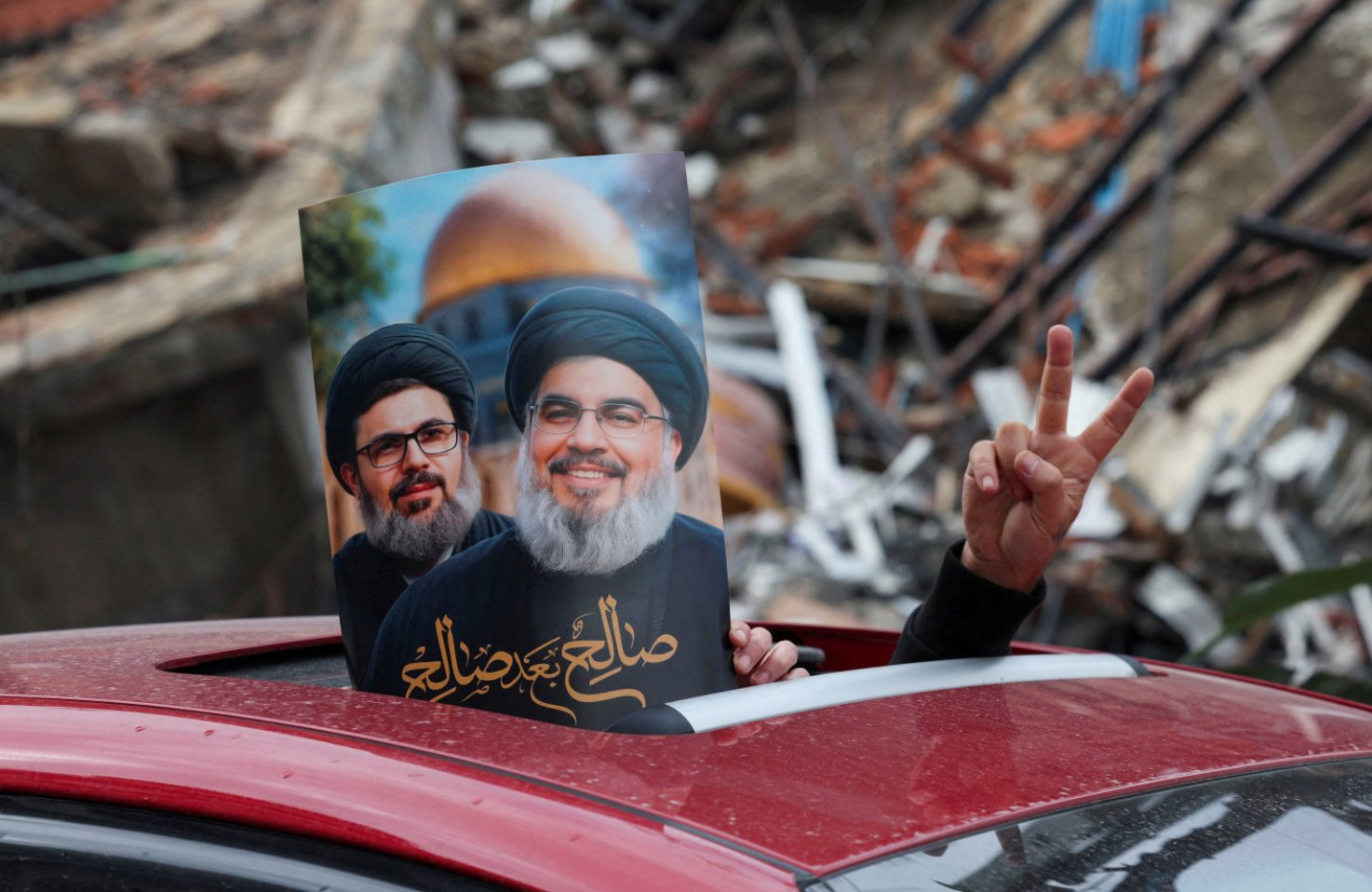 Tanda kemenangan dan poster dengan gambar mendiang pemimpin Hizbullah Sayyed Hassan Nasrallah dan mendiang pejabat senior Hizbullah Hashem Safieddine tampak di luar jendela atap mobil di pinggiran selatan Beirut.