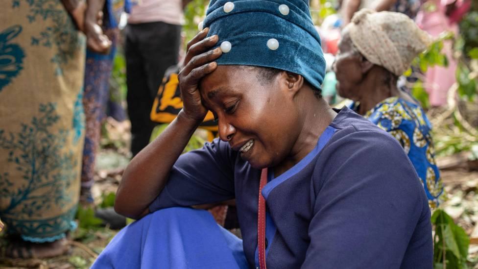 Una mujer llora desconsolada sentada en la tierra durante el funeral de los estudiantes