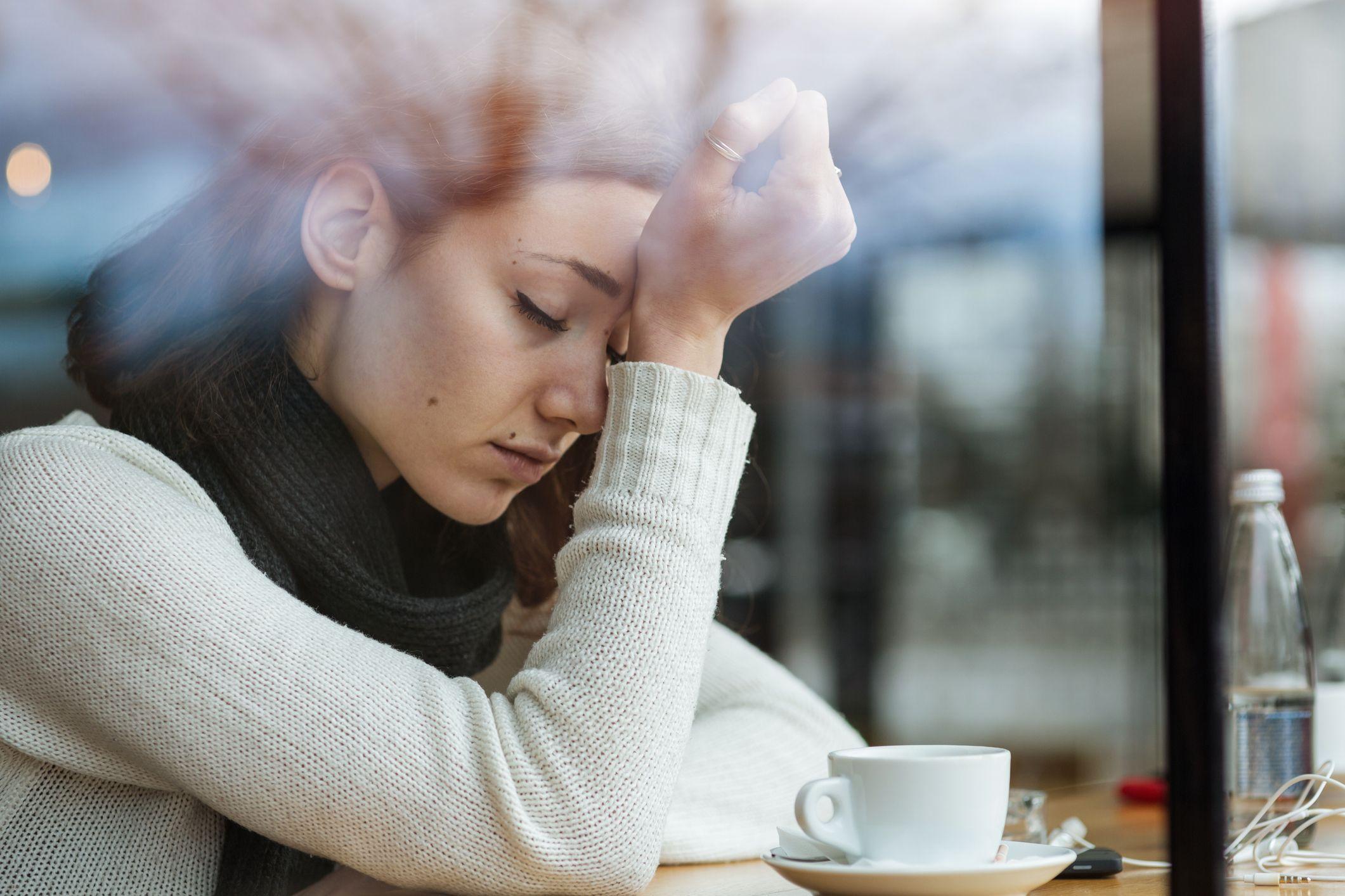 Una mujer con dolor de cabeza frente a una taza de café