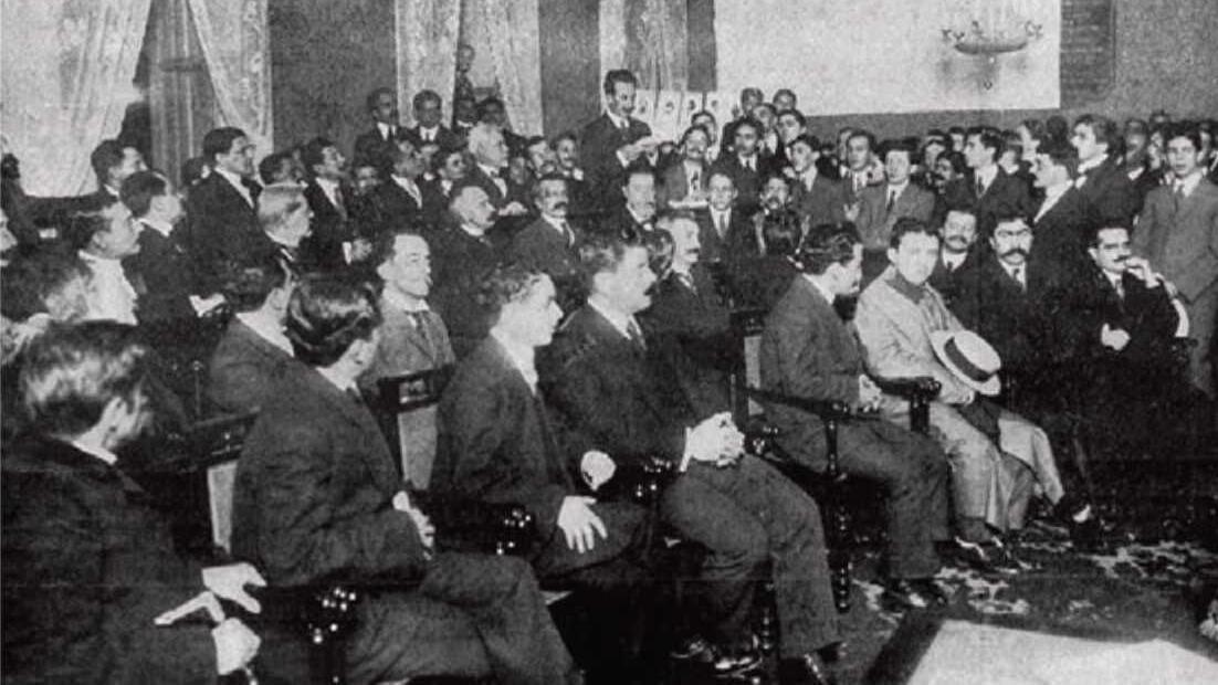 Em foto de 1911 publicado pelo jornal O Malho, de autor desconhecido, Carlos Chagas está apresentando sua pesquisa à Academia Nacional de Medicina. 