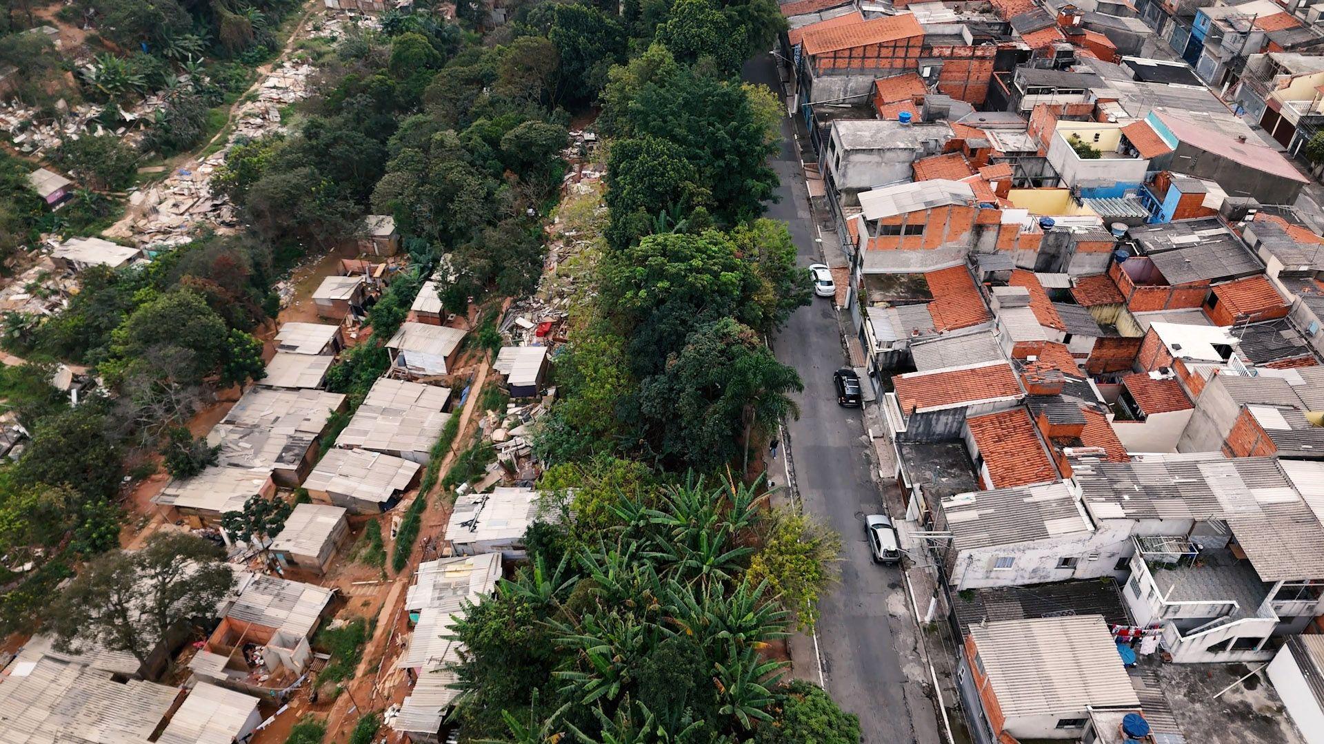 Vista aérea dos barracos de Veneza City em meio às árvores (à esquerda). Do lado direito, uma fileira de casas do mutirão 26 de julho