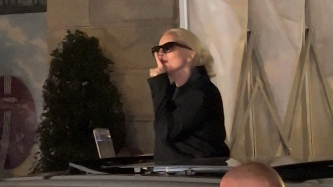 Lady Gaga se lleva un dedo a los labios mientras se prepara para reproducir nueva música para sus fans desde su computadora portátil, afuera de un hotel en Francia