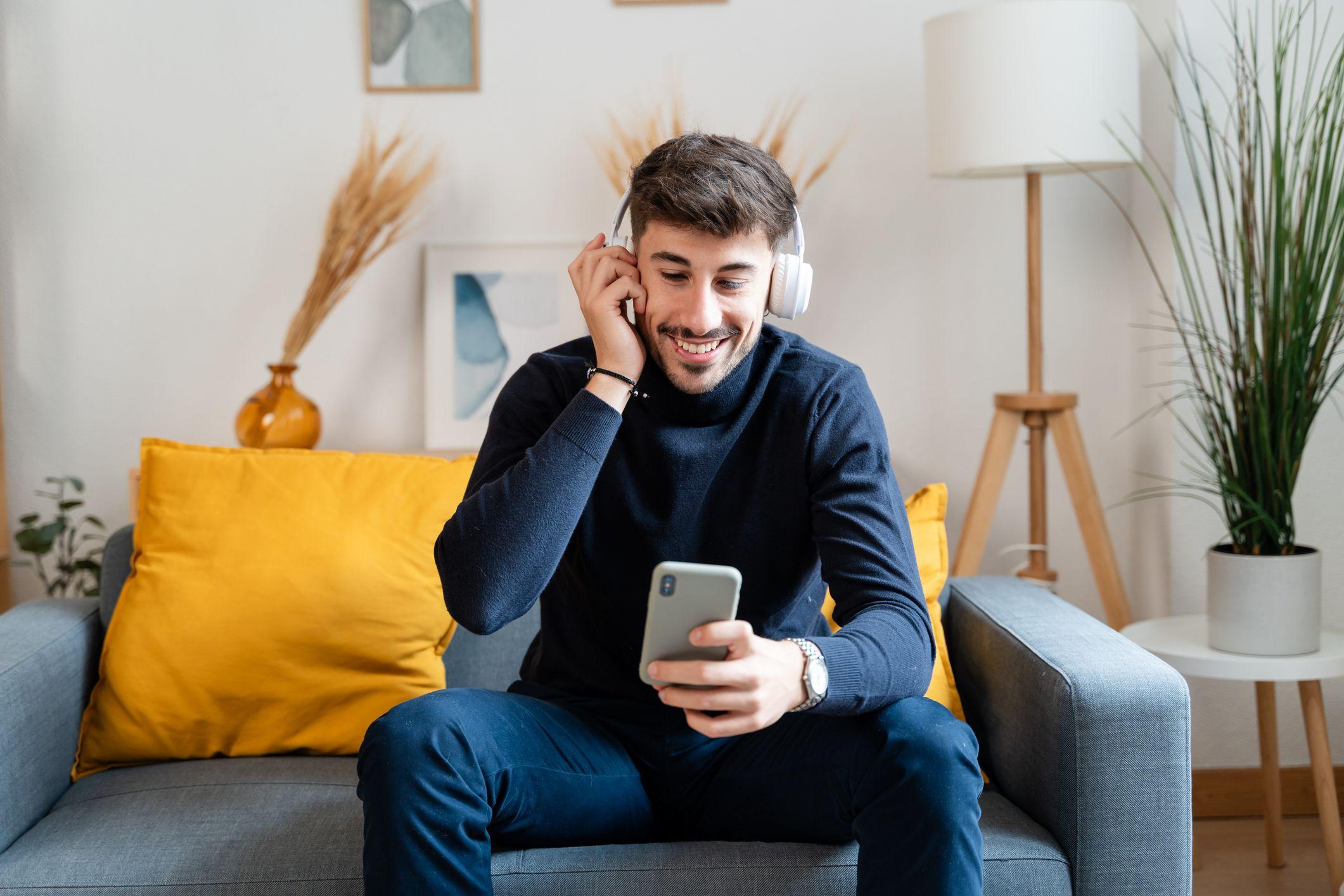 Homem sentado em sofá de fone de ouvido falando no celular.