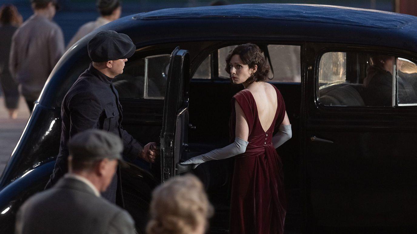 Una mujer se sube a un auto cuya puerta sujeta un hombre en una escena del film. 