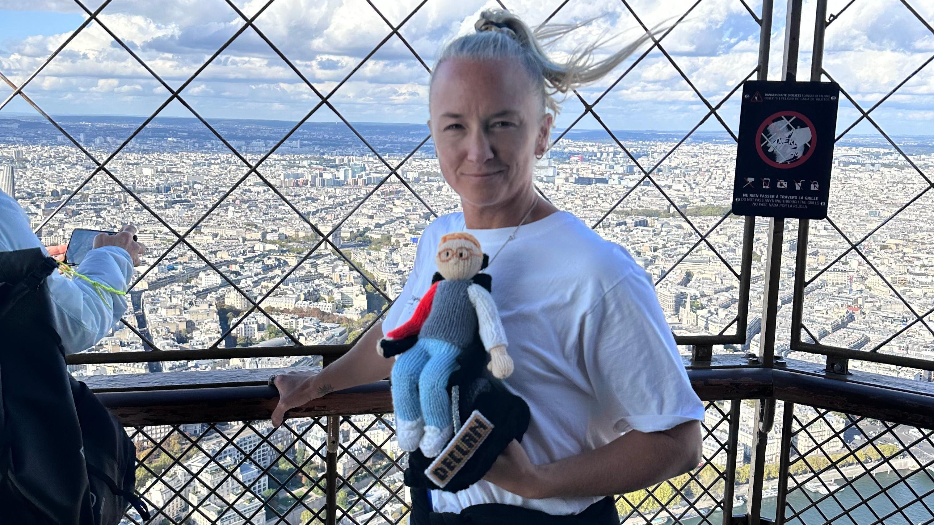 Alex está na plataforma de observação da Torre Eiffel, segurando uma versão tricotada de Declan