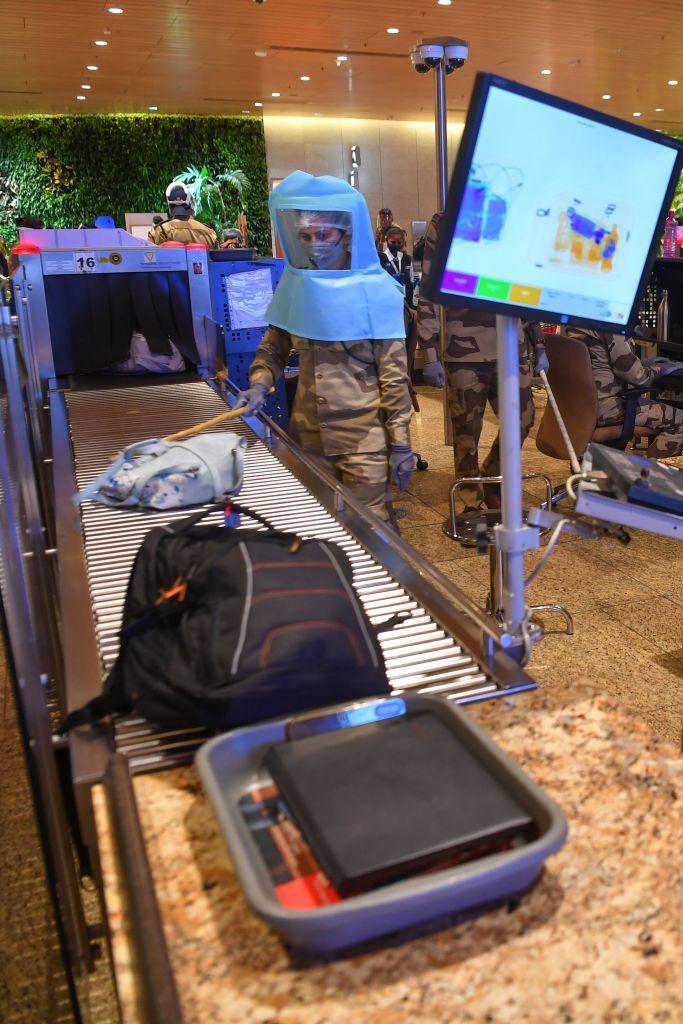 A Central Industrial Security Force (CISF) personnel wearing Personal Protective Equipment (PPE) uses a stick to move hand baggage at a security check of the Chhatrapati Shivaji Maharaj International Airport (CSMIA)