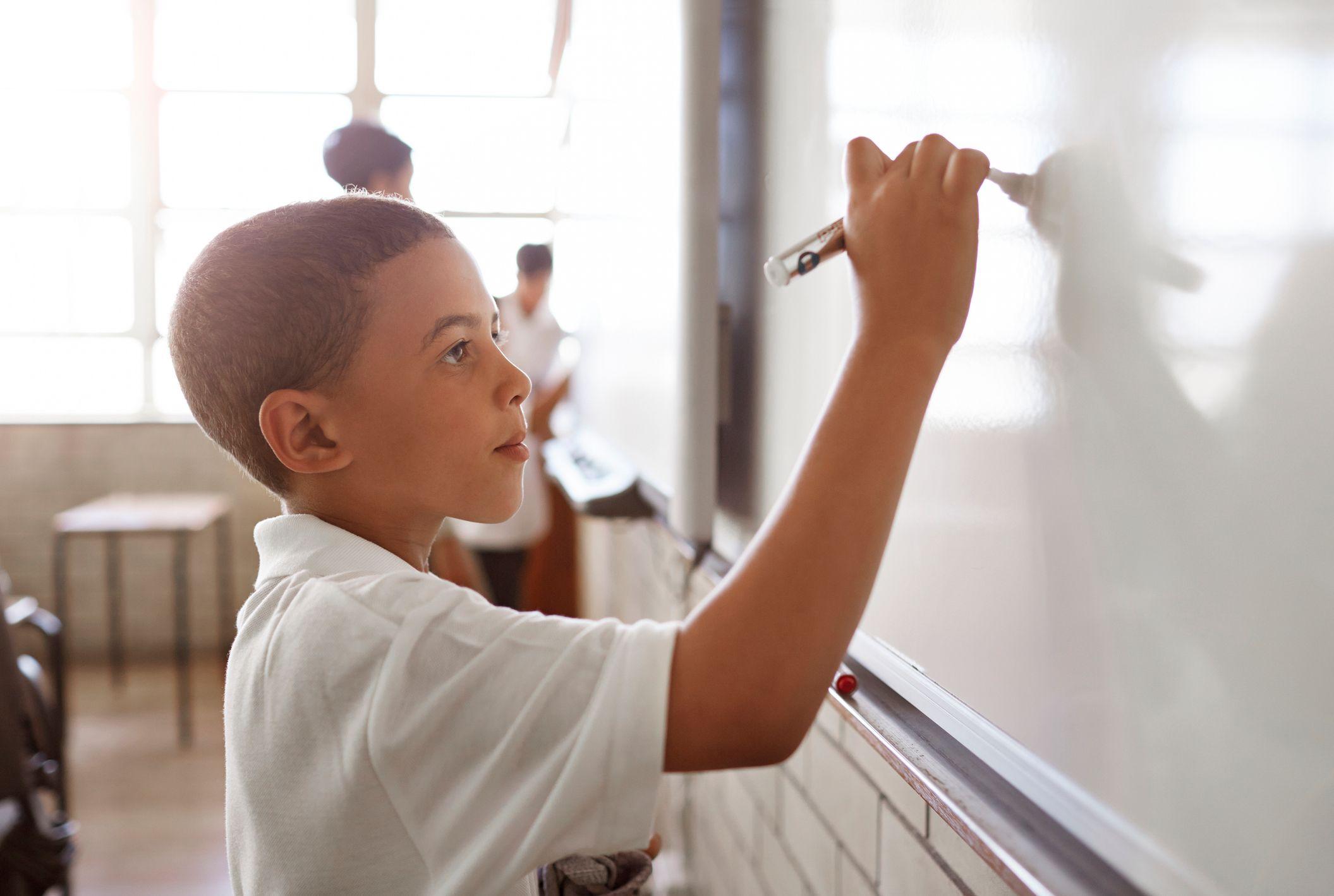 Niño escribiendo en el pizarrón de un aula.