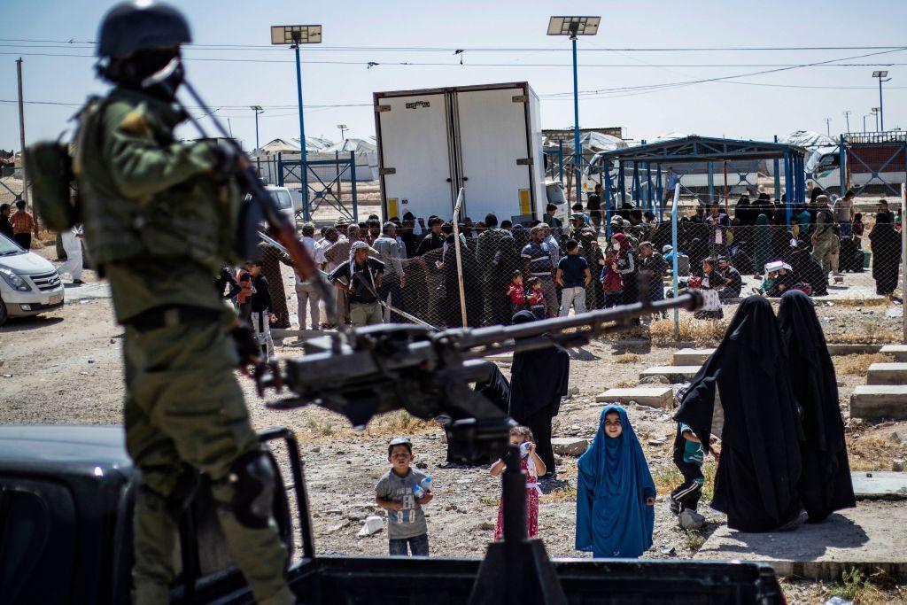 عضو بقوات أمن كردية يحرس مخيم الهول الذي يضم أقارب مقاتلي تنظيم الدولة بينما تستعد مجموعة من المحتجزين المفرج عنهم لمغادرته، سبتمبر 2023