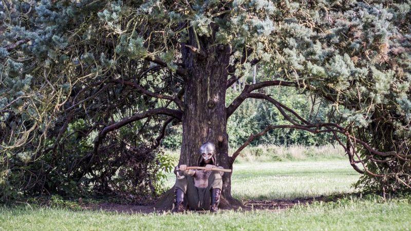 Homem com máscara sentado diante de árvore