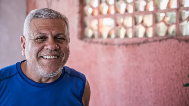 Homem de cabelo branco e camisa azul sorri