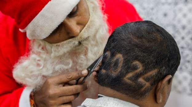 حلاق يرتدي ملابس بابا نويل يرسم رقم 2024 على رأس شخص في الهند