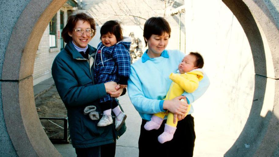 Portrait of a pair of unidentified, would-be adoptive mothers as they each pose with a baby, Beijing, China