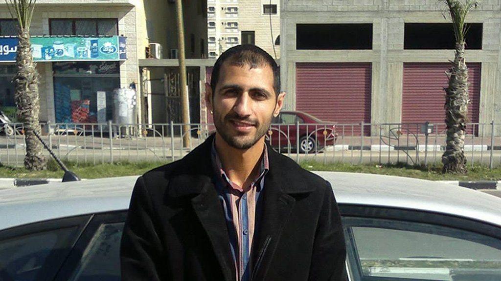 Mahmoud Shaheen vistiendo una chaqueta y camisa negra, de pie junto a un automóvil, en una calle.