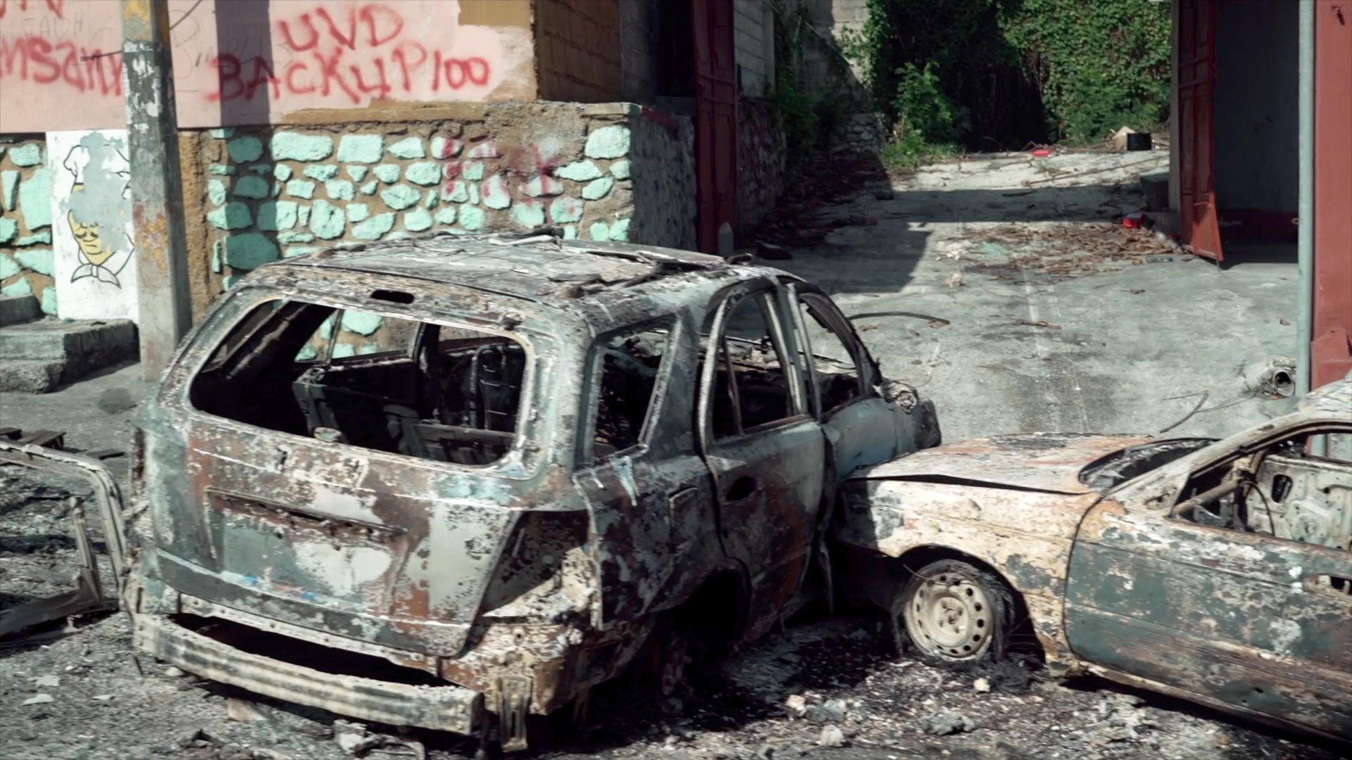 Dois carros queimados perto de uma parede com graffiti