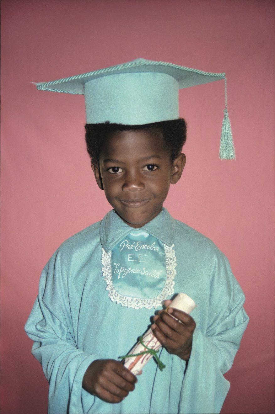 Menino posando para foto com roupa de formatura e segurando diploma