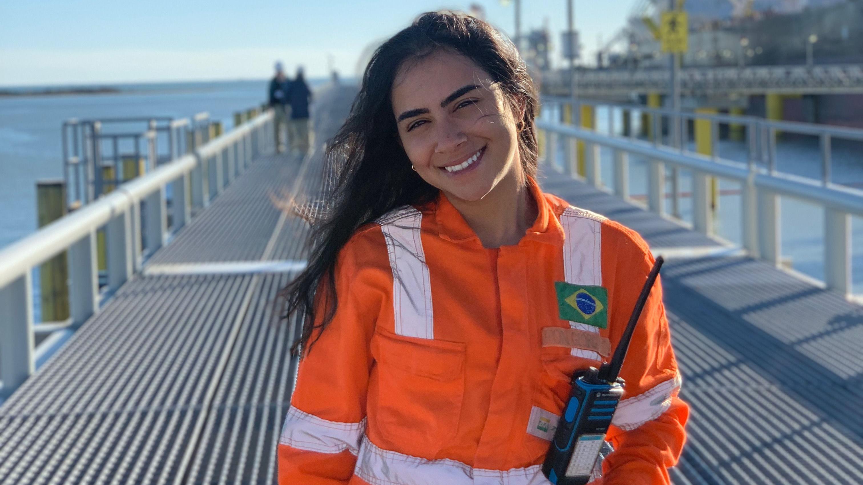 Geórgia sorrindo para foto, aparecendo em pé, uniformizada em um deck