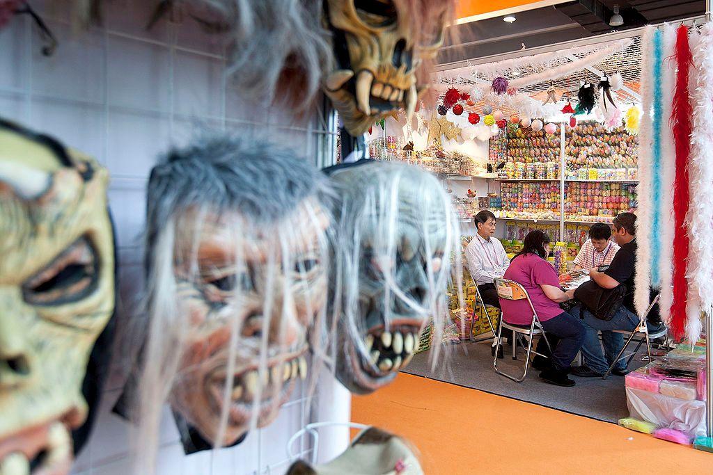 Máscaras expostas em pavilhão, com pessoas sentadas à mesa negociando atrás