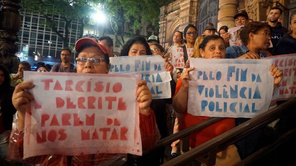 Mulheres seguram cartazes pedindo fim da violência policial no dia 5 de dezembro