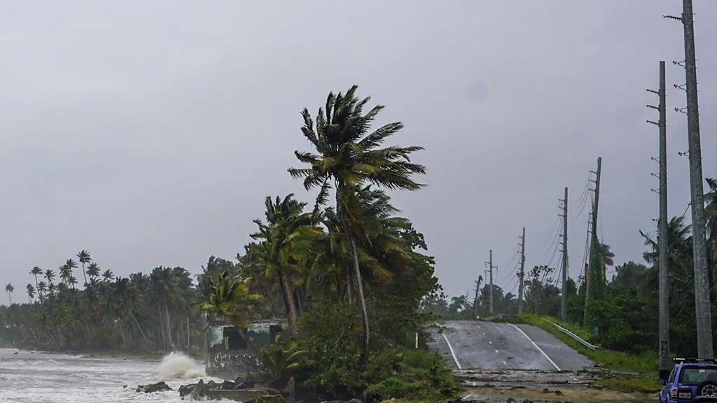 Foto de uma tempestade. Do lado esquerdo, o mar com ondas revoltas. No meio da imagem, árvores em ventania. Do lado direito, uma estrada.