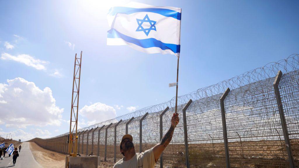 Um homem segura uma bandeira israelense na travessia de fronteira de Nitzana, em Israel