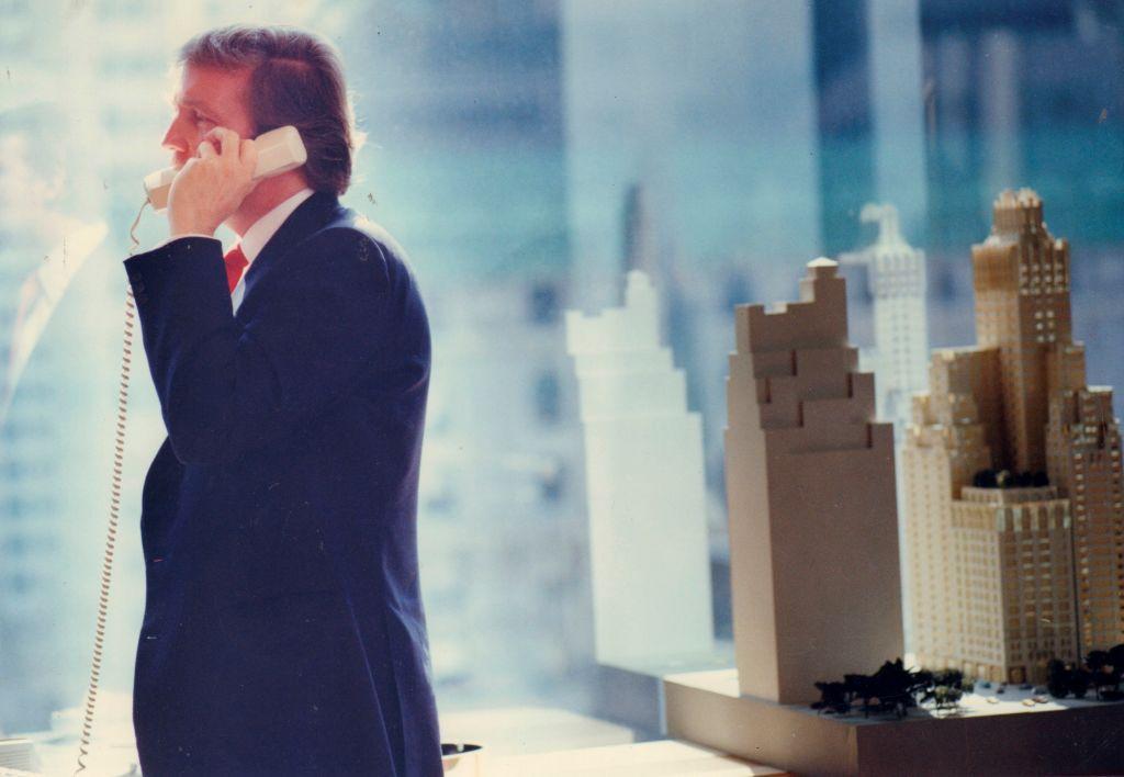 Donald Trump habla por teléfono desde su oficina en Trump Plaza en Manhattan en 1987. Hay una maqueta de un rascacielos al lado 