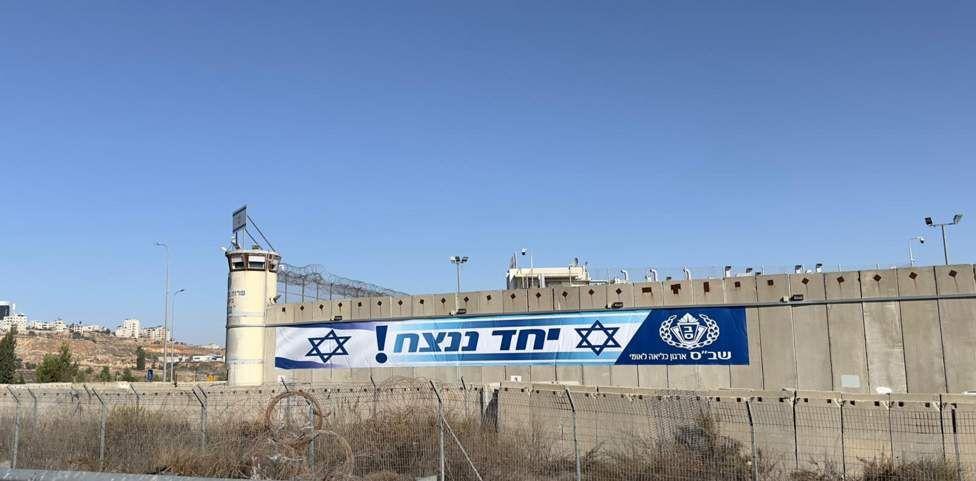Una pancarta colgando de una infraestructura con la frase “¡Unidos triunfaremos!” y la bandera de Israel