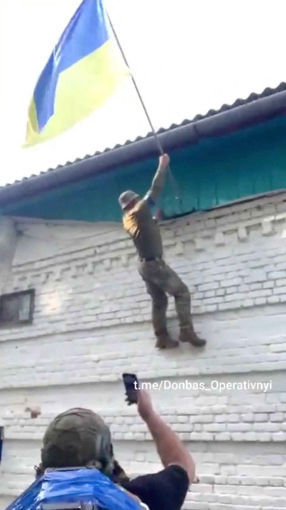 Un soldado ucraniano coloca la bandera de su país en el ayuntamiento de una aldea invadida.