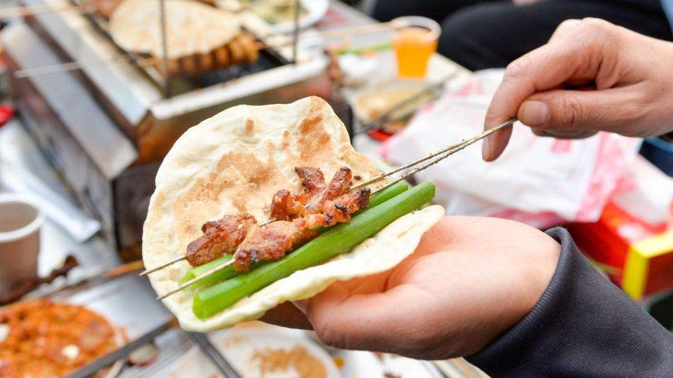 바비큐 꼬치와 채소를 얇게 부쳐 낸 밀가루 반죽에 싸 먹는 모습