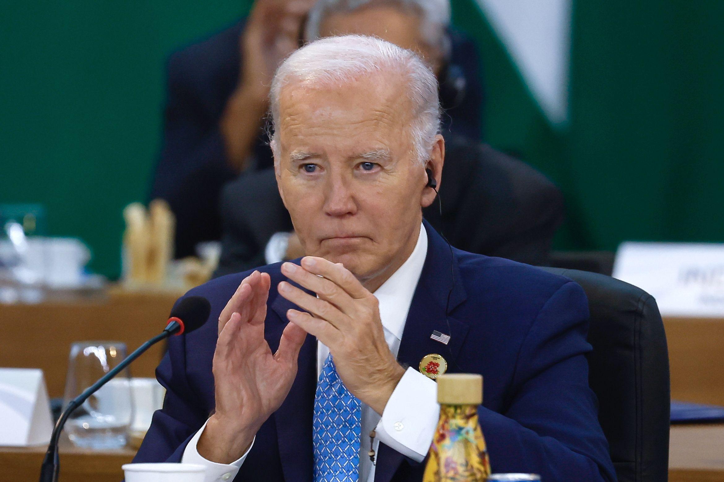 Biden aplaudindo, sentado diante de mesa em conferência