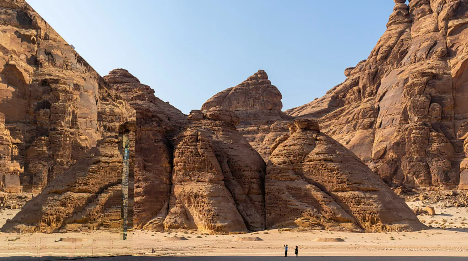 Construção espelhada no deserto, rodeada por pessoas e rochas