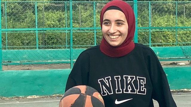 Una mujer con velo sonríe mientras mantiene un balón de baloncesto en la mano.