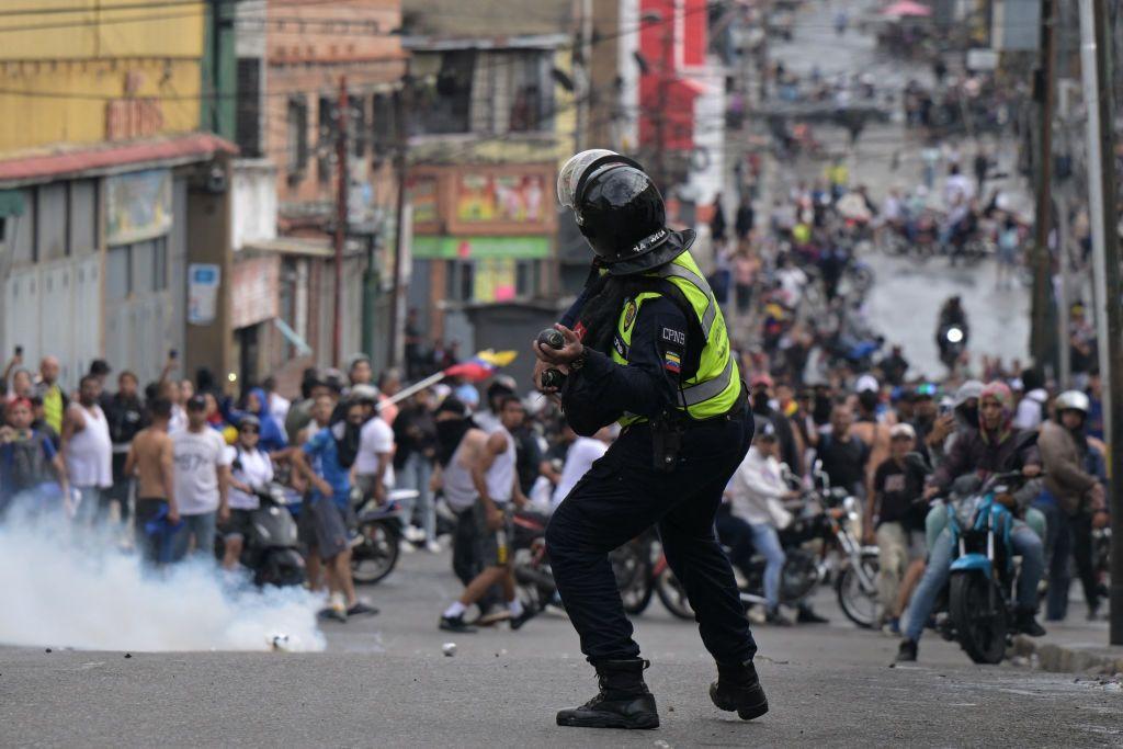 Un policía lanzando una bomba de gas a unos manifestantes
