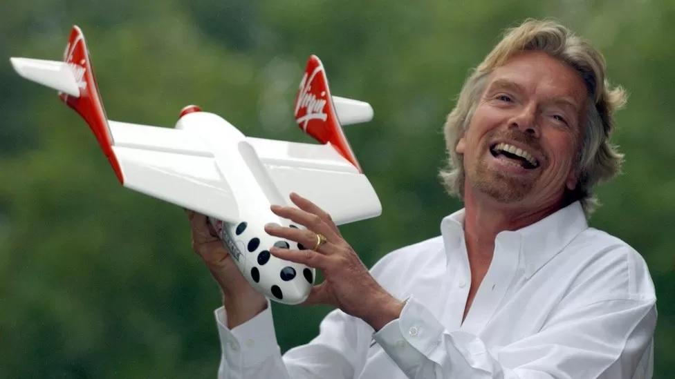 Richard Branson, um homem branco de camisa branca, segunrando um foguete