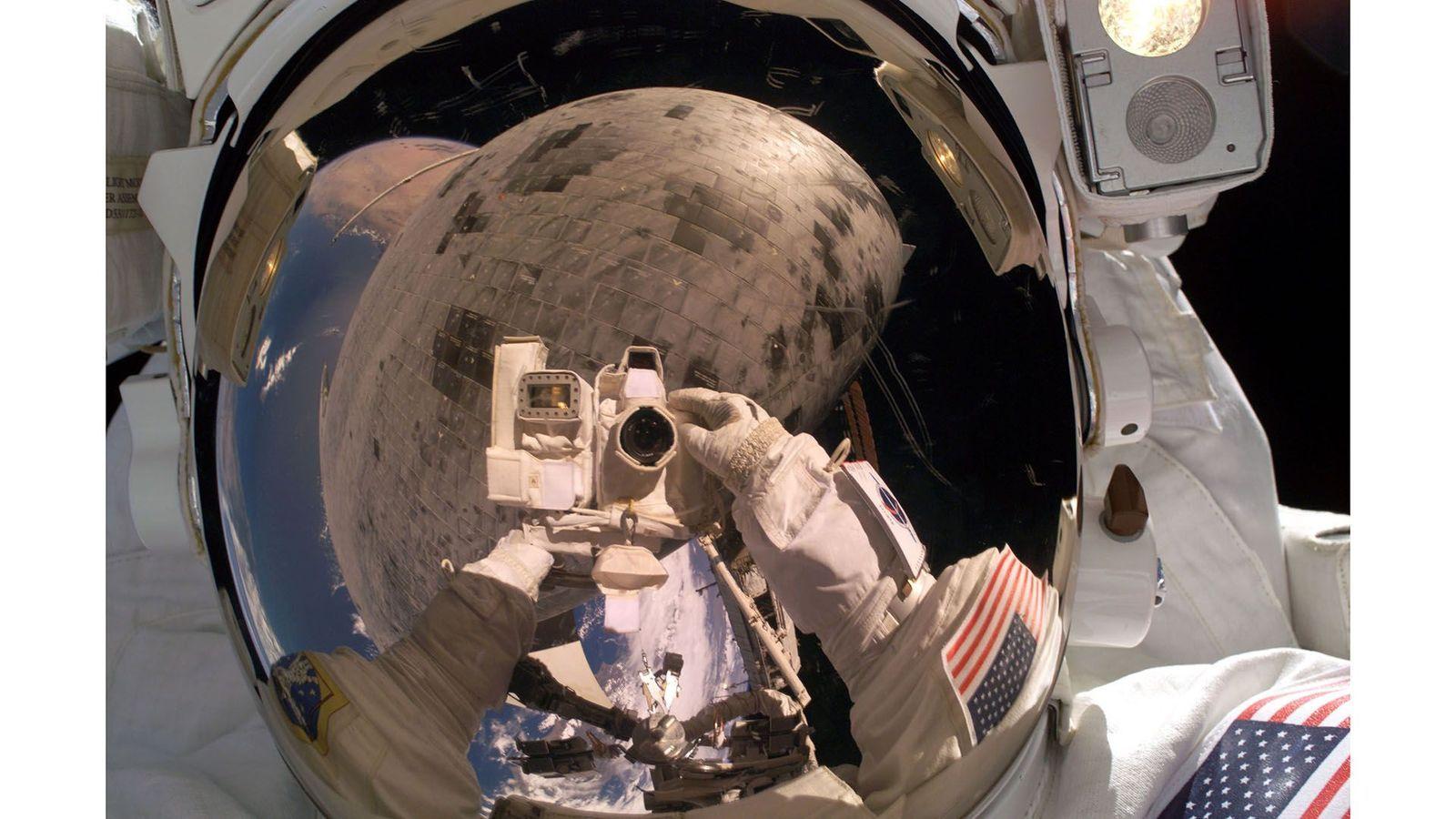 Reflexo de astronauta segurando câmera e trabalhando no espaço é visível na viseira do capacete