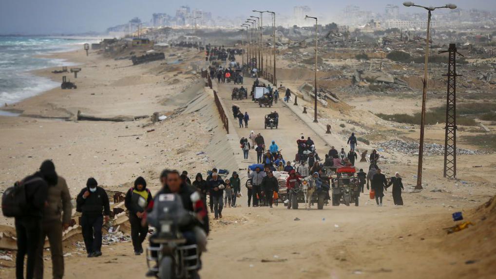 Desplazados en la Franja de Gaza caminan o circulan en motos cerca de la playa