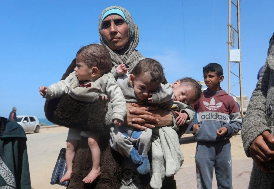امرأة فلسطينية تهرب من مستشفى الشفاء عقب غارة إسرائيلية، وهي تحمل أطفالها الثلاثة أثناء تحركها جنوباً