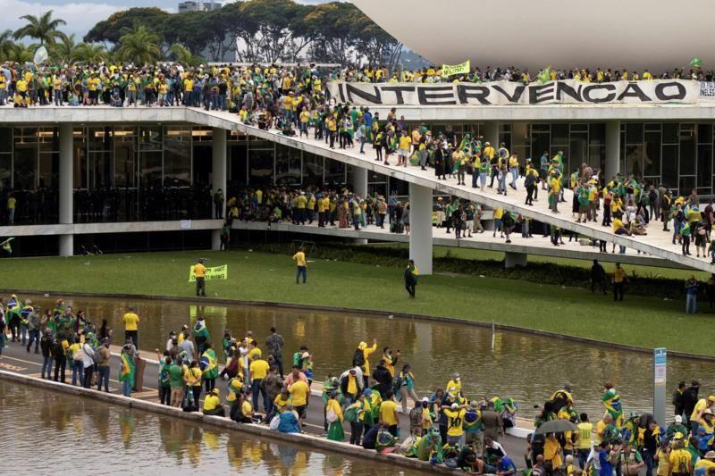 Centenas de apoiadores de Jair Bolsonaro invadem o prédio do Congresso Nacional. Eles aparecem usando roupas com as cores verde e amarelo e carregando bandeiras do Brasil. Há uma faixa no topo do prédio escrito: Intervenção