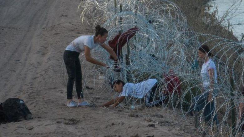 Una familia de migrantes intenta pasar a través de un alambre de concertina en Eagle Pass el 27 de julio.