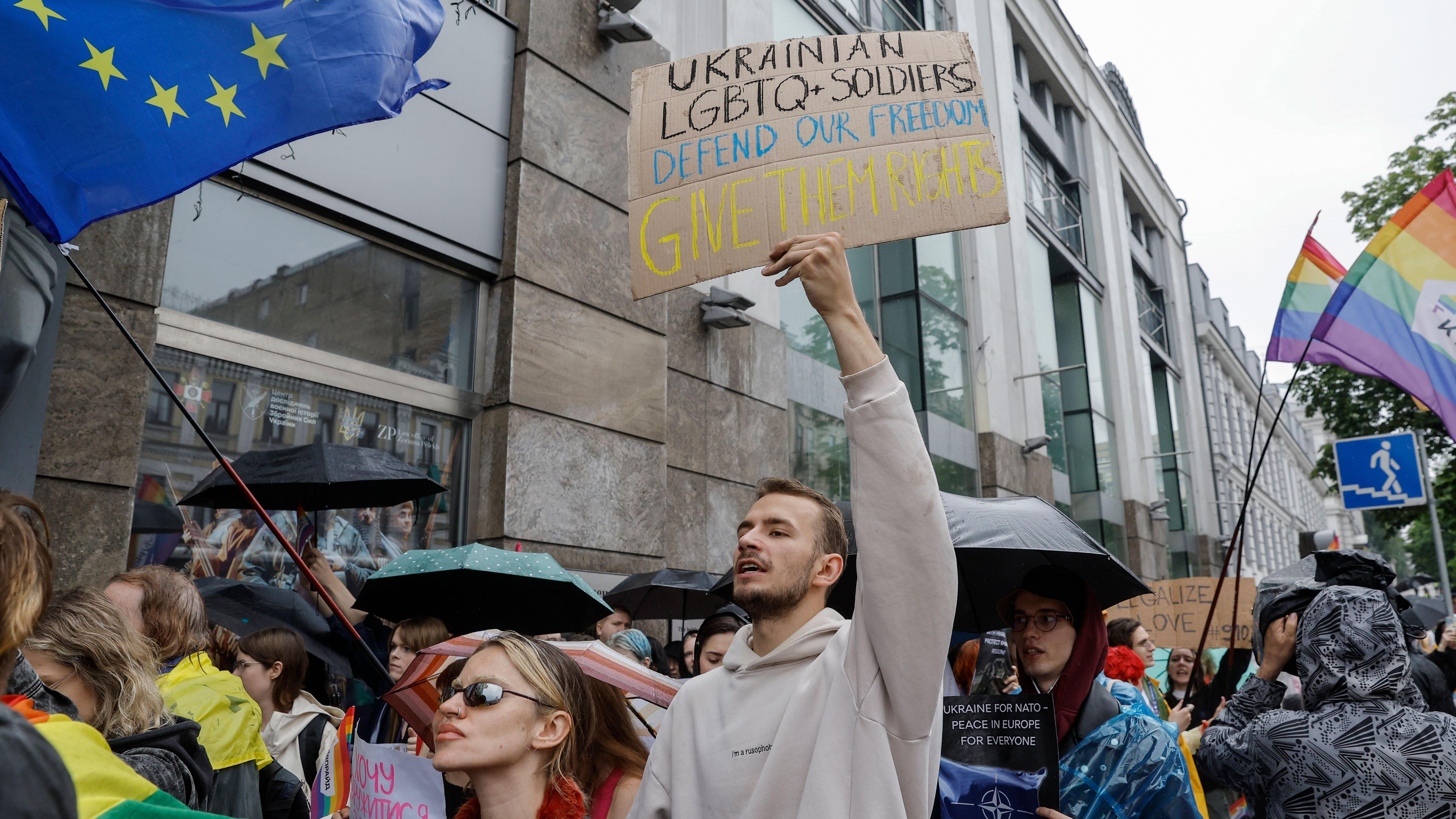 Pessoas na marcha do Orgulho, incluindo um homem segurando uma placa que diz 