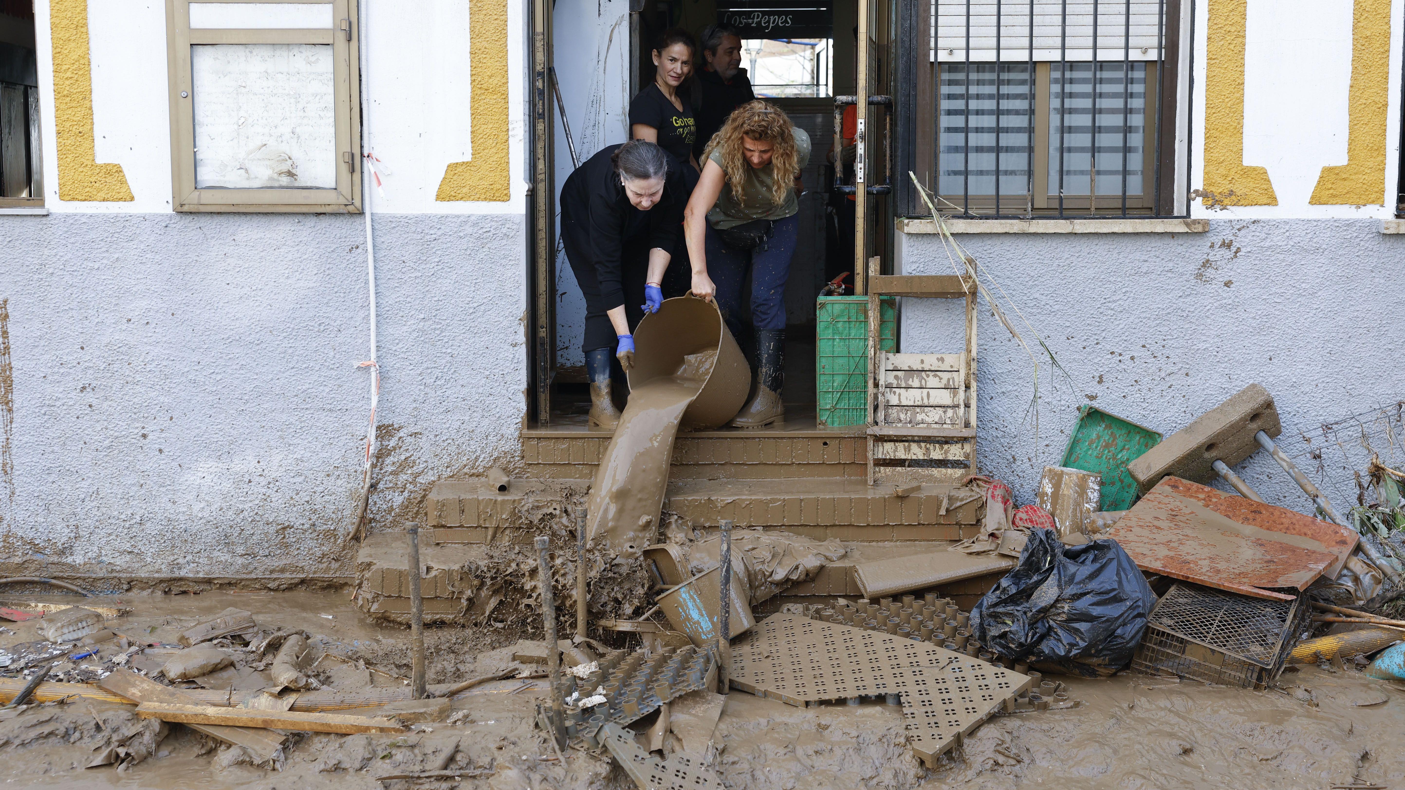 Unas mujeres achican agua y barro de una peluquería. 