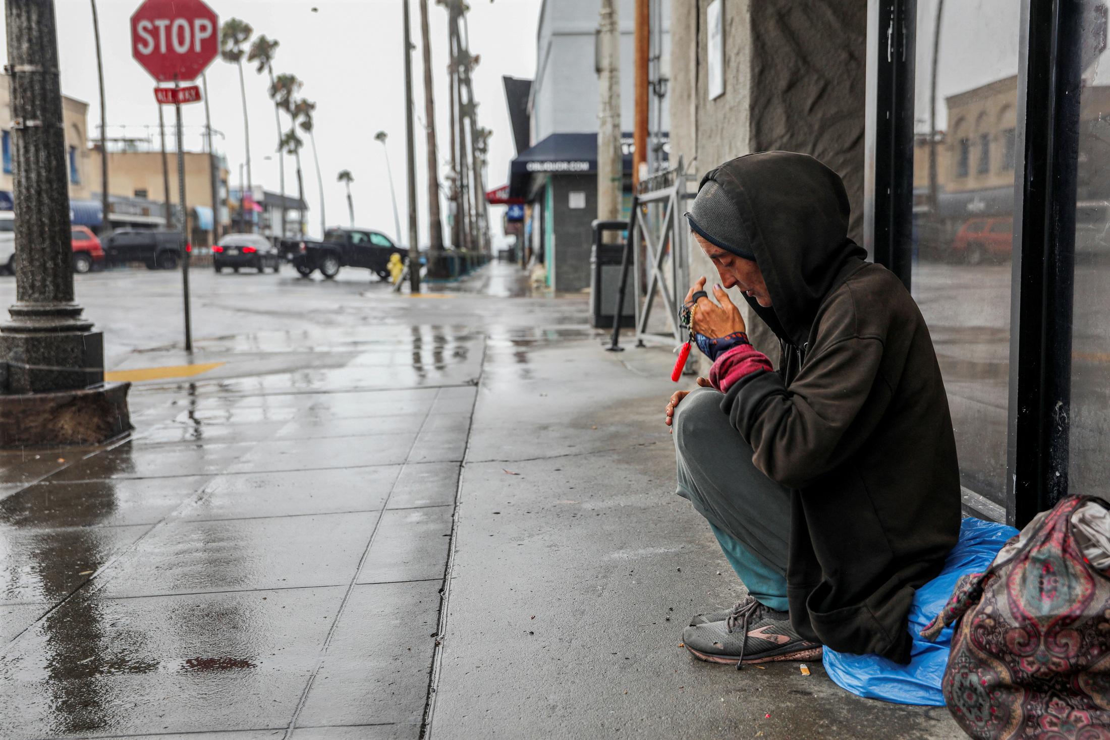 Una mujer sin hogar sentada en la vereda de Newport Avenue en el área de Ocean Beach de San Diego (California)mientras la tormenta tropical Hilary se acerca.