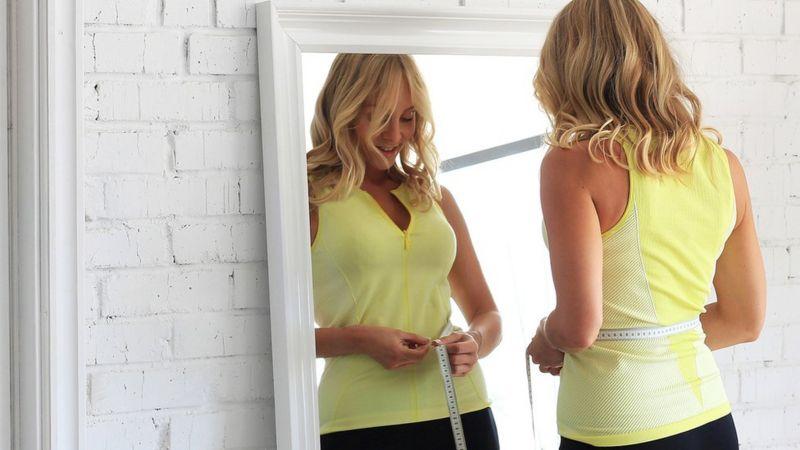 Mulher medindo a cintura em frente ao espelho