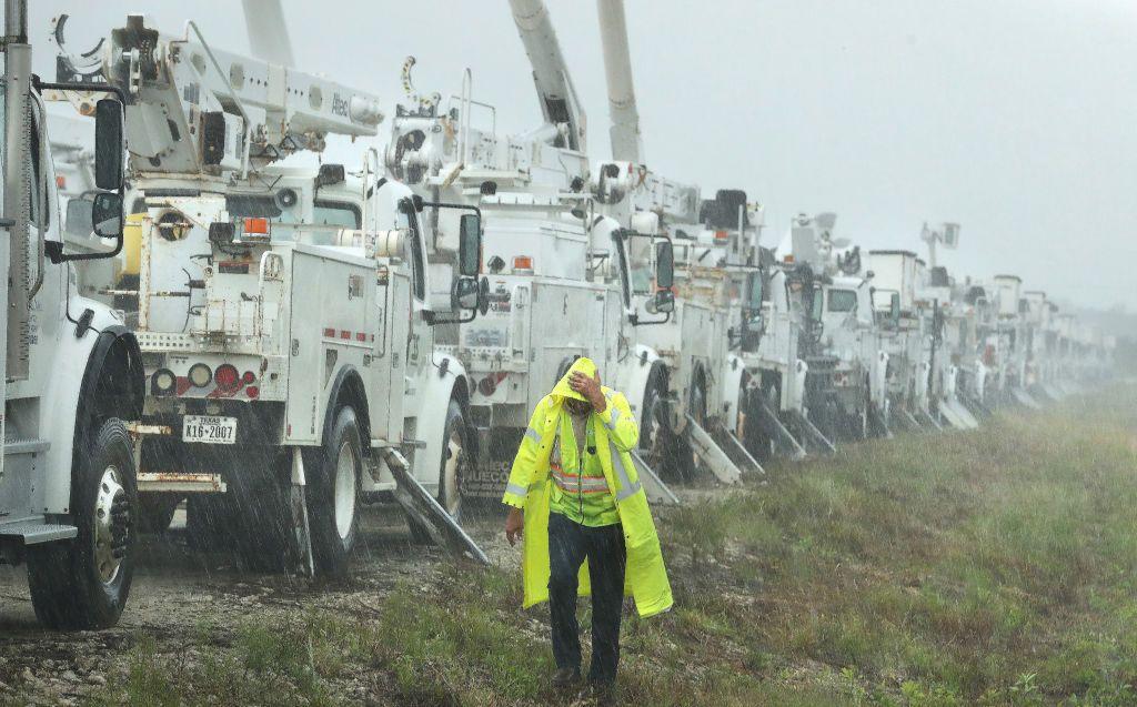 A Fishel lineman takes on torrential rain as he walks past a line of power line trucks in a field in The Villages, Florida.